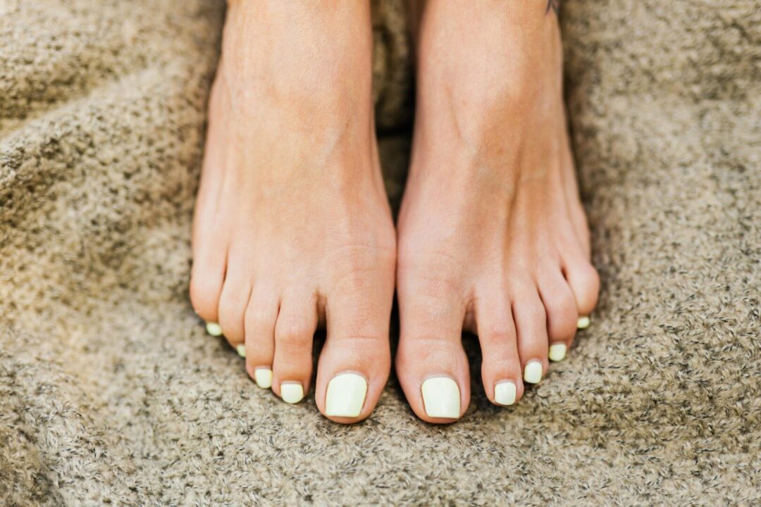 Aesthetic close-up of feet with painted toenails resting on a textured carpet.